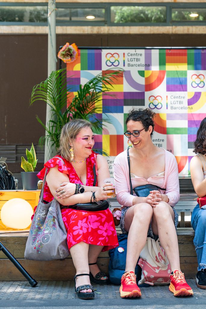 Dues noies assegudes amb el fotoreclam al darrera de la festa del Centre LGTBI