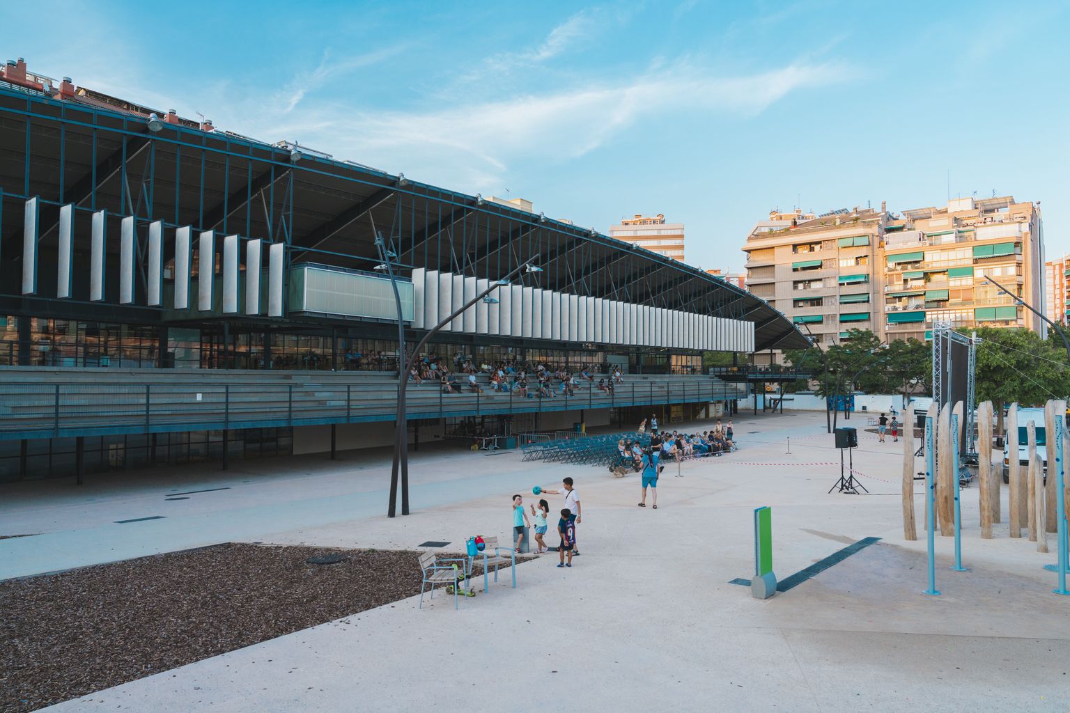 Exterior del Canòdrom i de la plaça del Canòdrom amb els espais preparats per assistir a una sessió de cinema a la fresca. A la plaça es veuen unes cadires i hi ha grups d'infants jugant