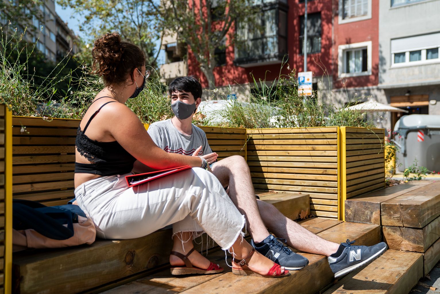 Dos joves de l’Institut Viladomat conversen asseguts a les jardineres amb bancs instal·lades a la zona pacificada al voltant del centre educatiu