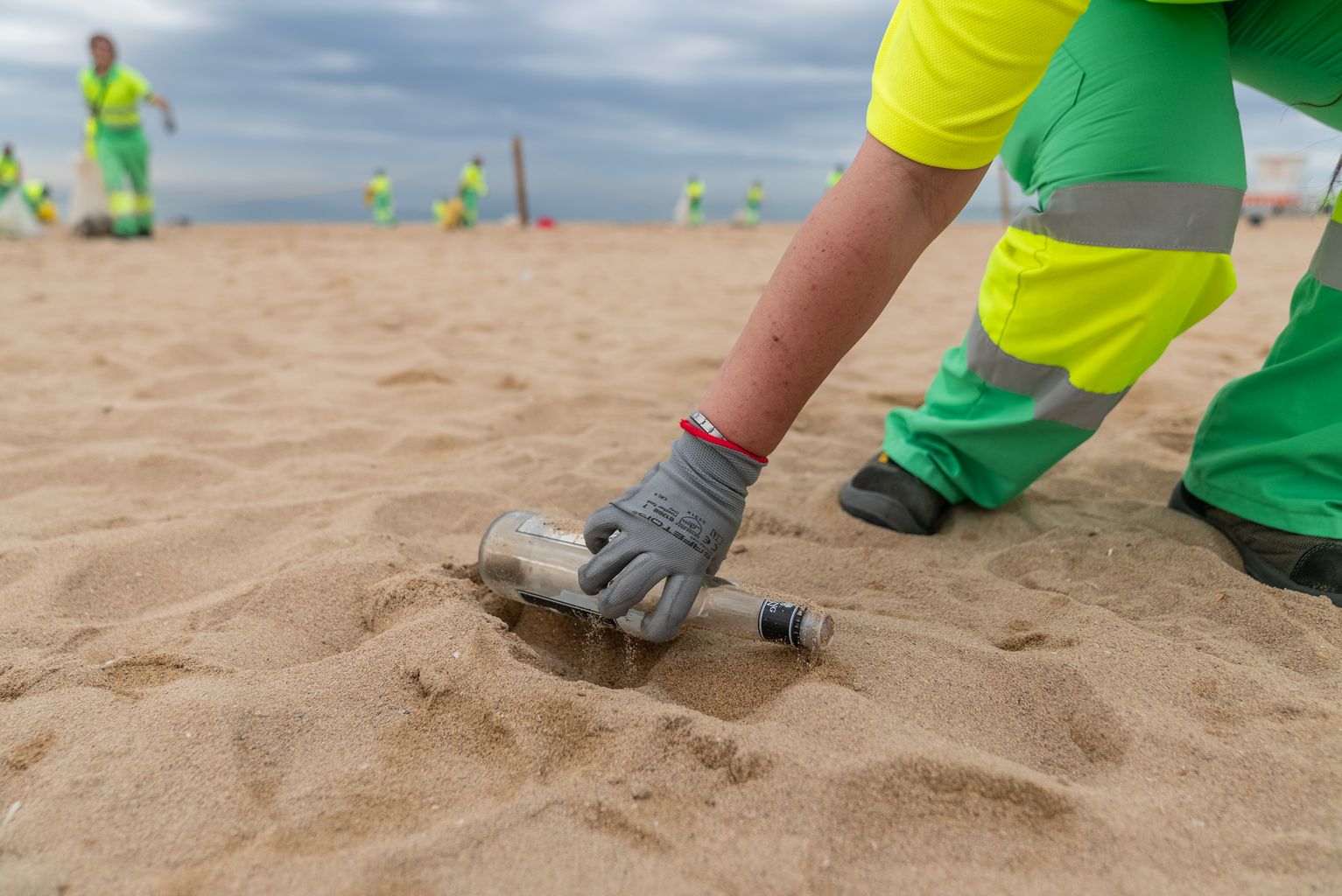 Un treballador del Servei de Neteja recull una ampolla de vidre de la sorra de la platja durant el dispositiu especial després de la revetlla de Sant Joan.