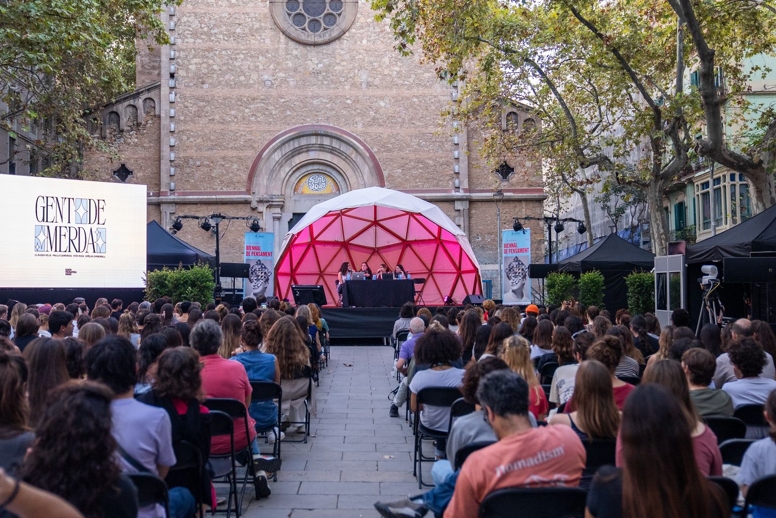 Plano general de la charla "Bienal. Vivir en Barcelona: Gente de mierda en directo", con Clàudia Rius, Paula Carreras, Rita Roig y Ofèlia Carbonell, en la plaza de la Virreina con el público asistente escuchando atentamente