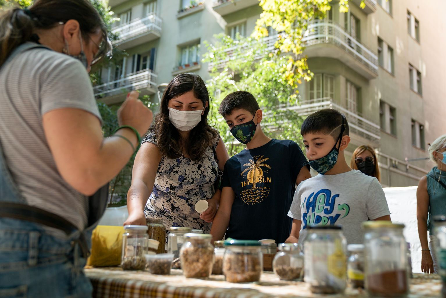 Infants i grans escoltant les explicacions del taller ”Fem boletes de llavors: nenodango”, a la Festa Major de Gràcia