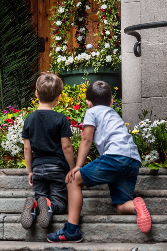 Uns infants miren l'ou com balla a la plaça de la Virreina on hi ha una font decorada i envoltada de flors elaborats amb motiu de la festa del Corpus davant de les portes de l'església de Sant Joan