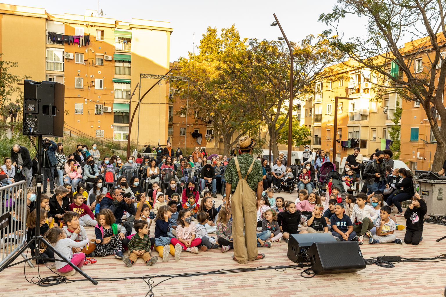 Gent asseguda al terra seguint un espectacle de circ durant la inauguració de la reurbanització de l'espai públic de l'interior d'illa del carrer d'Aiguablava