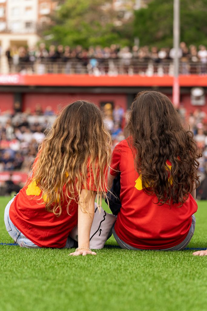 Dues nenes, membres d’equips del Club Esportiu Martinenc, assegudes durant l’acte d’inauguració de la nova gespa i presentació dels equips del club