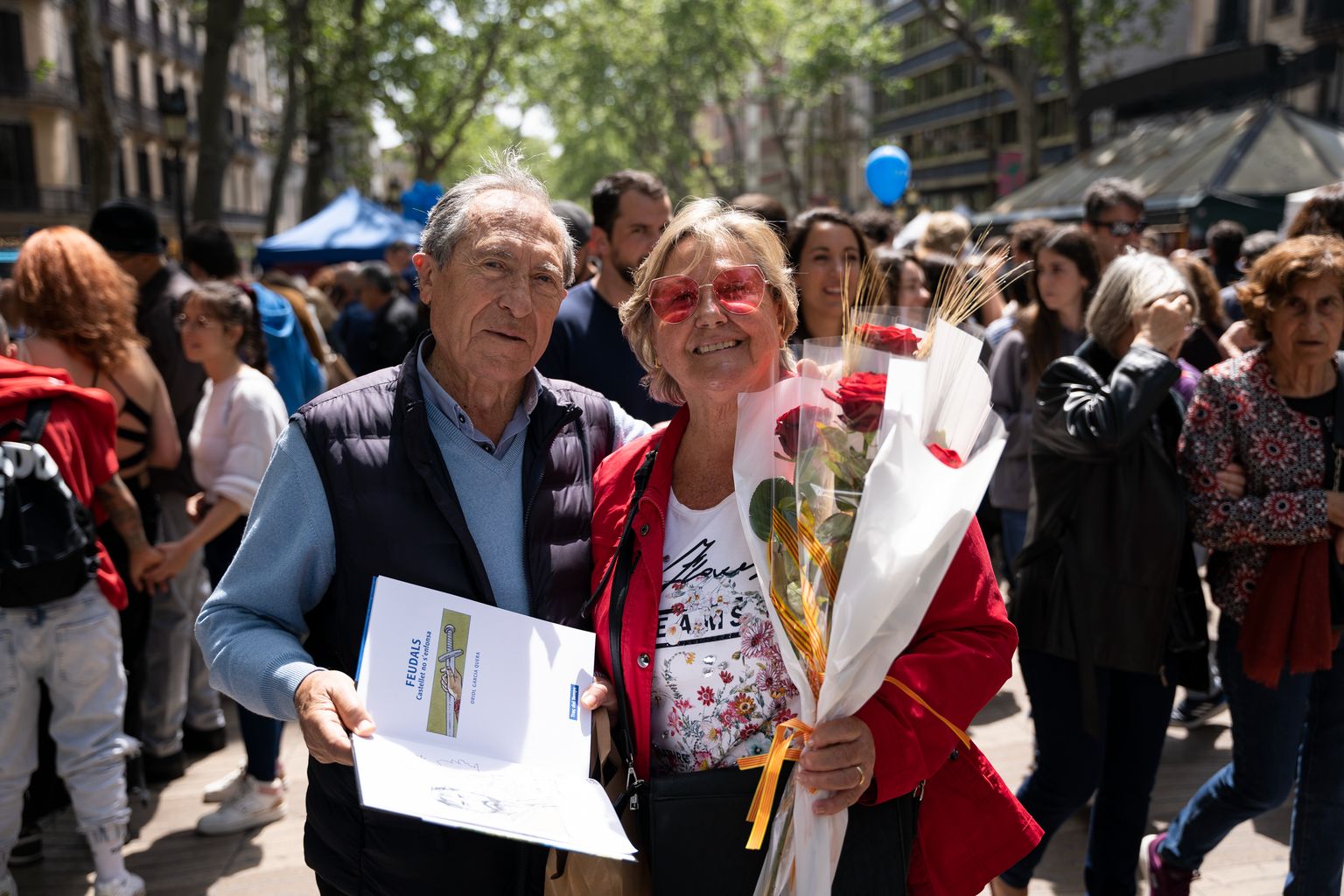 Una parella de persones grans mostren el llibre i la rosa que s'han regalat amb motiu de Sant Jordi.