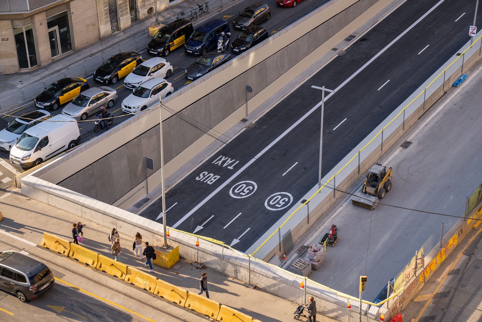 Vista de detall de l'accés al túnel de soterrament de la Gran Via de les Corts Catalanes en el tram de la plaça de les Glòries Catalanes al carrer de Castillejos amb el sentit Llobregat-Besòs ja enllestit però tancat encara a la circulació. Es veuen vianants creuant el carrer