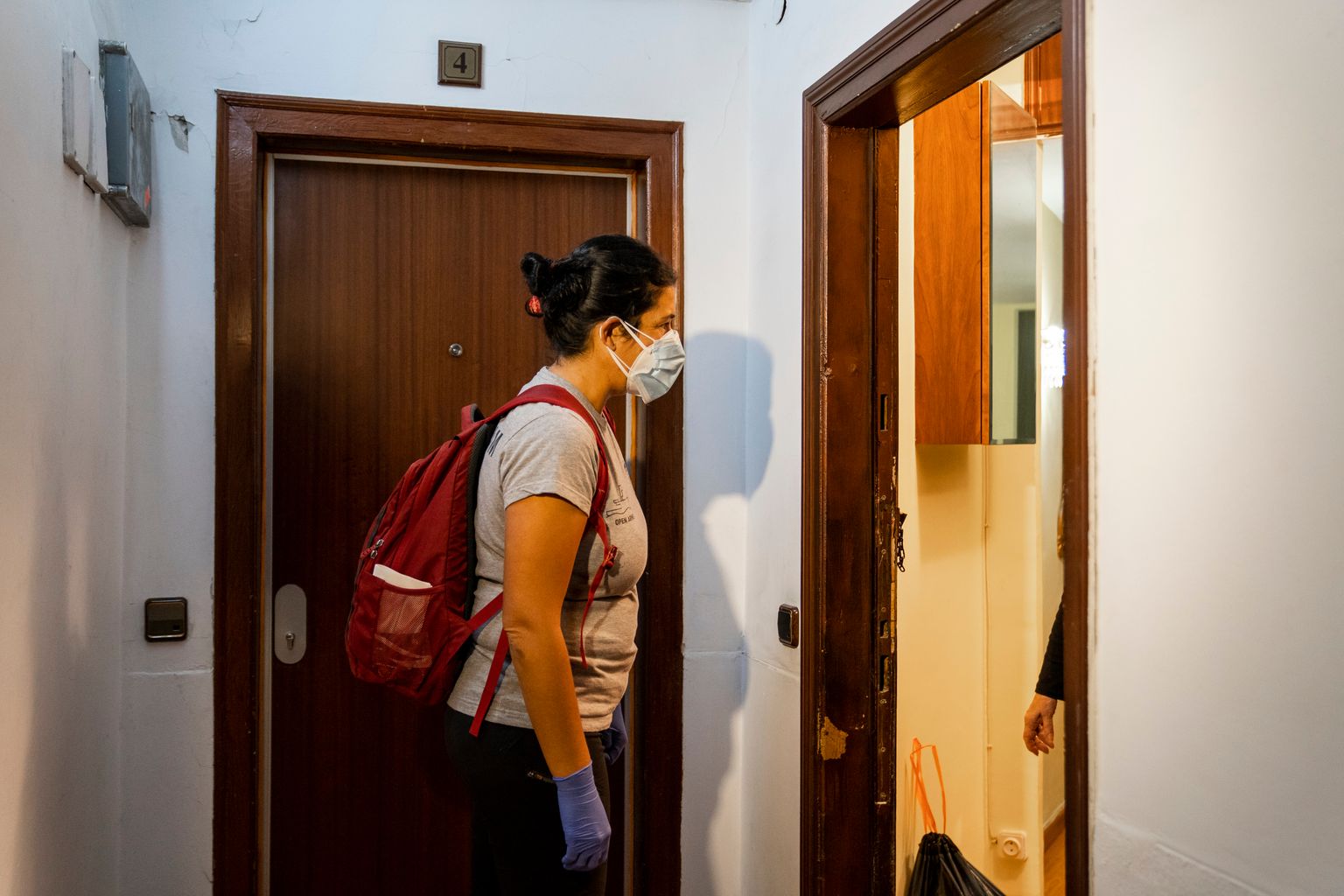 Una membre de l'ONG Open Arms, degudament protegida amb guants i mascareta, al replà d'un edifici on una dona li obre la porta