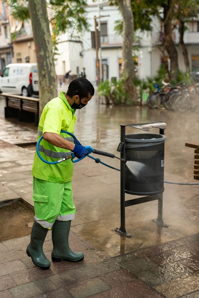 Un treballador del Servei de Neteja renta una paperera amb aigua a pressió