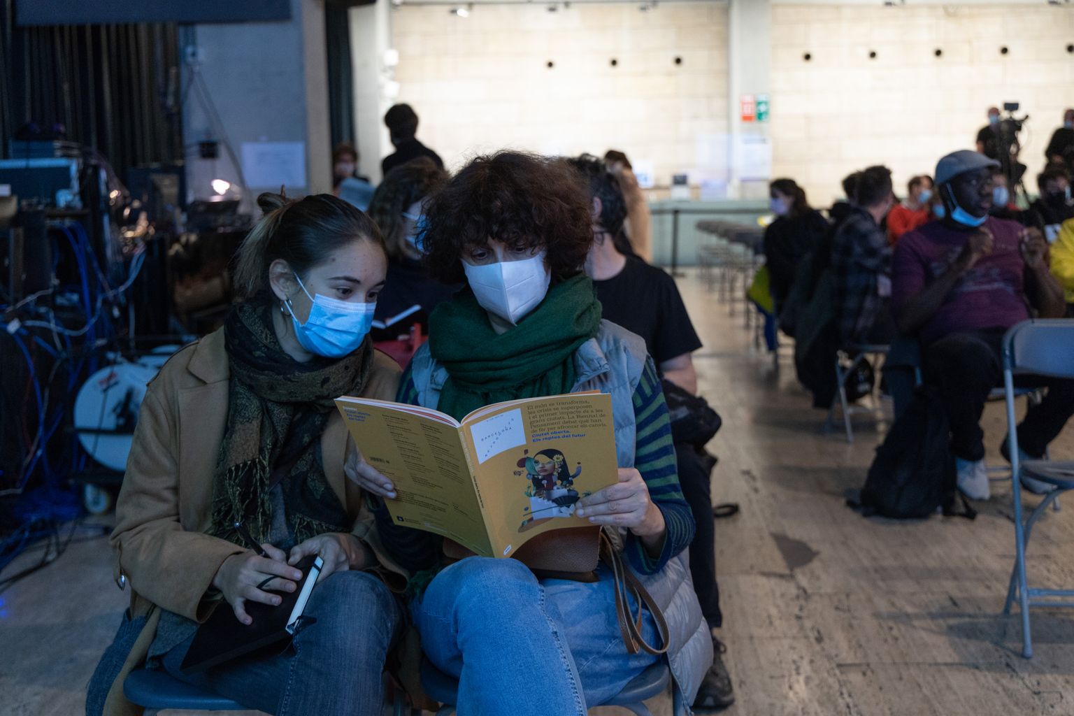 Dues dones del públic assistent a la taula rodona "El mirall del racisme" consulten el llibret amb el programa de la Biennal de pensament