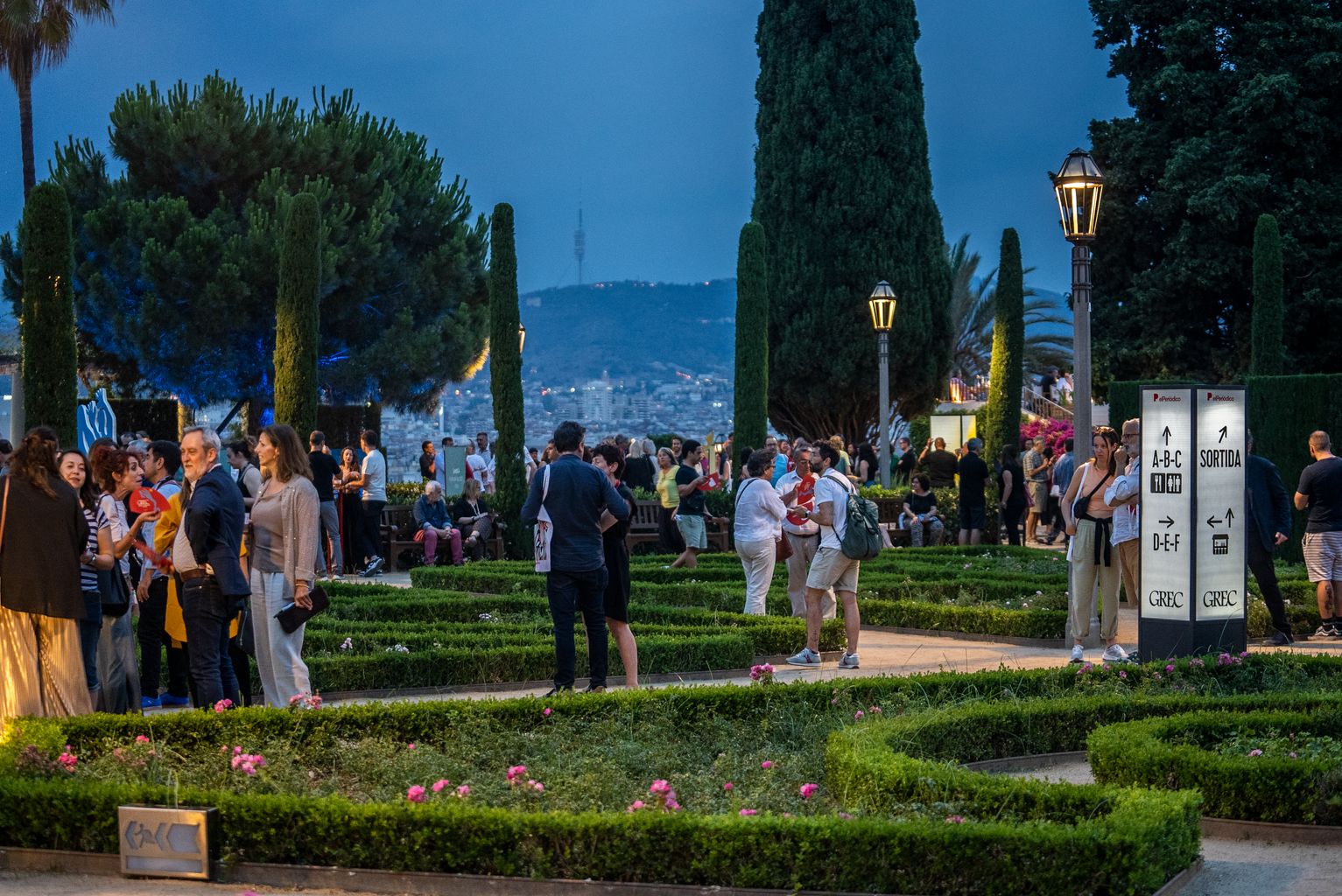 Persones conversant entre els jardins del teatre Grec. De fons, vistes de la ciutat i la Torre de Collserola.