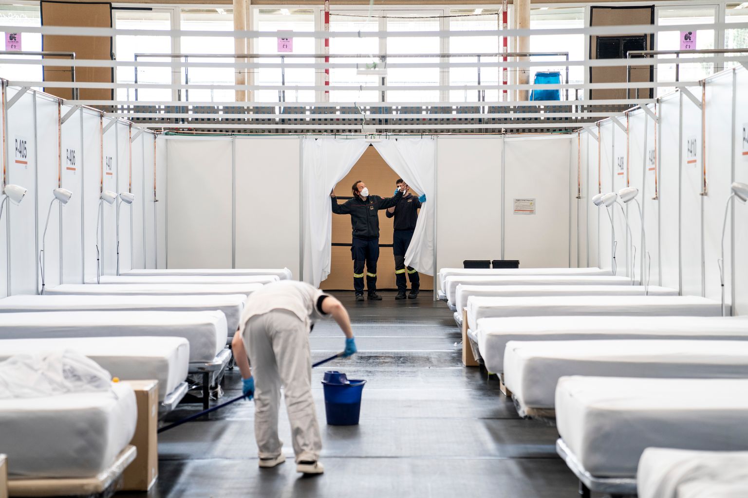 Personal sanitari de neteja frega el terra d’un dels pavellons amb llits. Al fons, dos agents de Bombers miren l’adequació dels espais del Pavelló Salut Guinardó