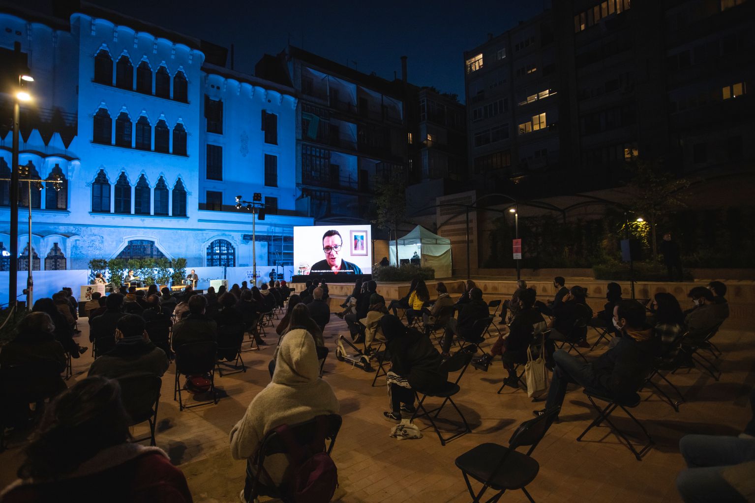 Taula rodona "Quanta participació pot suportar la democràcia?" als jardins d'Agustí Centelles. Vista del públic i de la pantalla on es pot seguir la intervenció telemàtica de Michele Della Morte