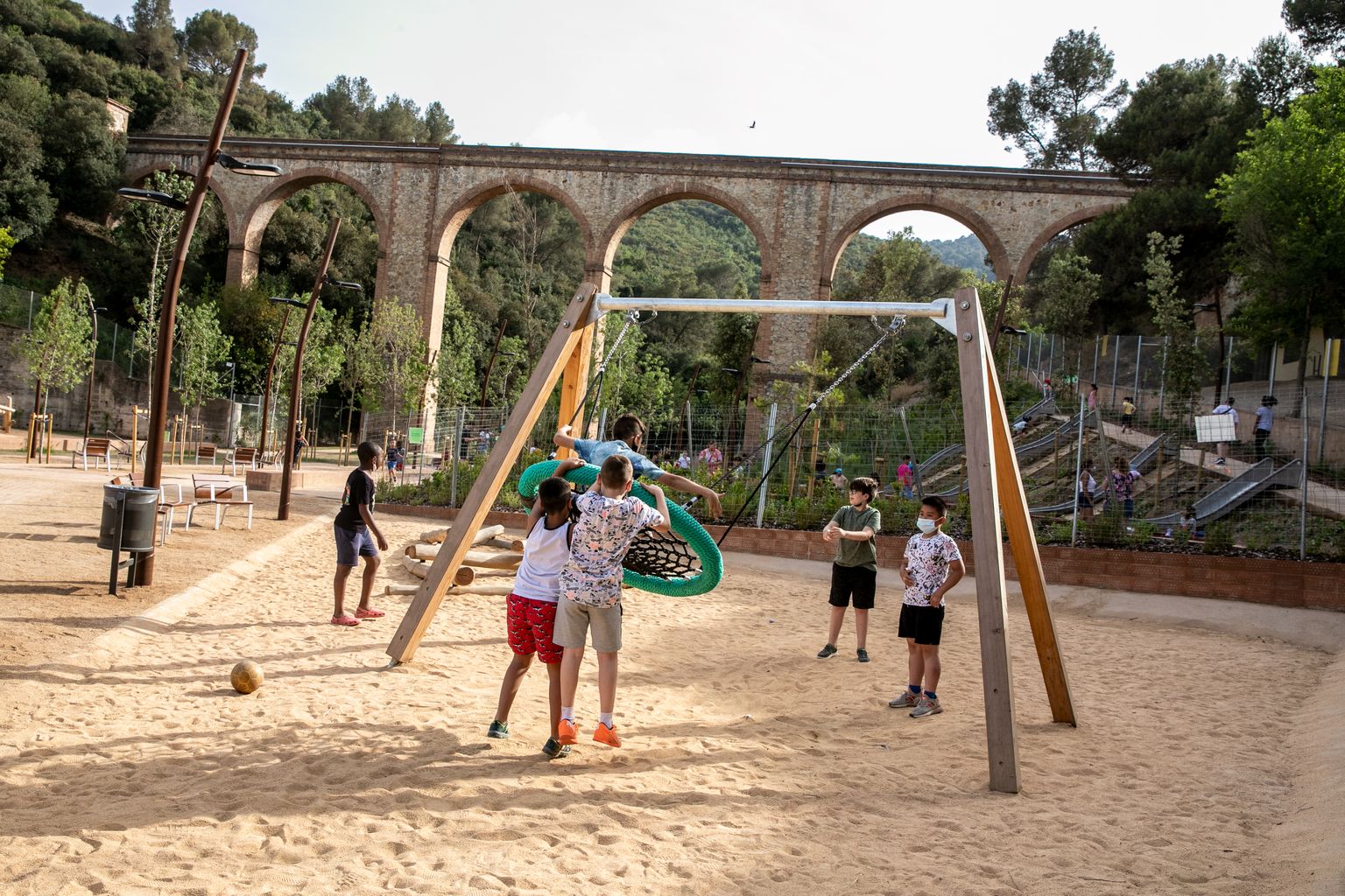 Área de juego infantil con columpios del parque del Aqüeducte con unos niños jugando
