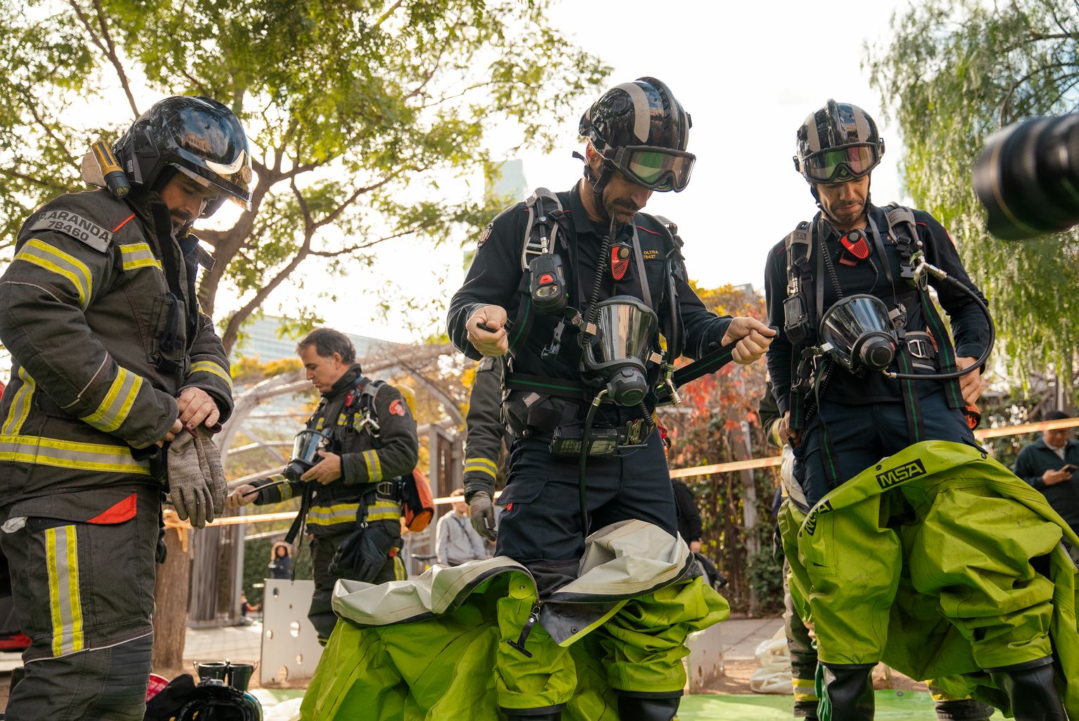 Tres bombers vestint-se amb un uniforme de protecció especial durant la demostració d’emergència química al parc Central del Poblenou