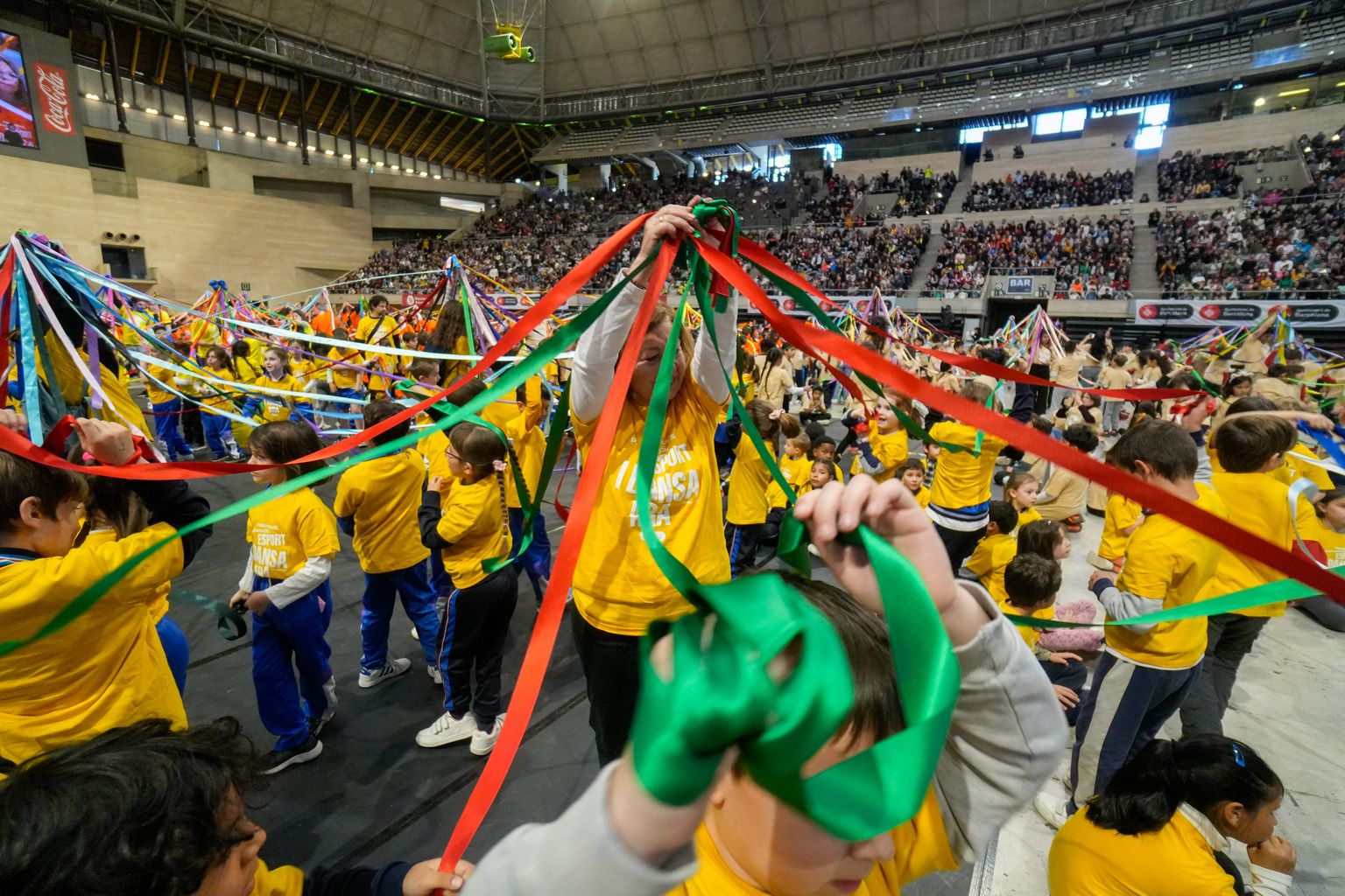 Infants ballant amb unes cintes de colors al voltant de la monitora durant el Dansa Ara 2024.