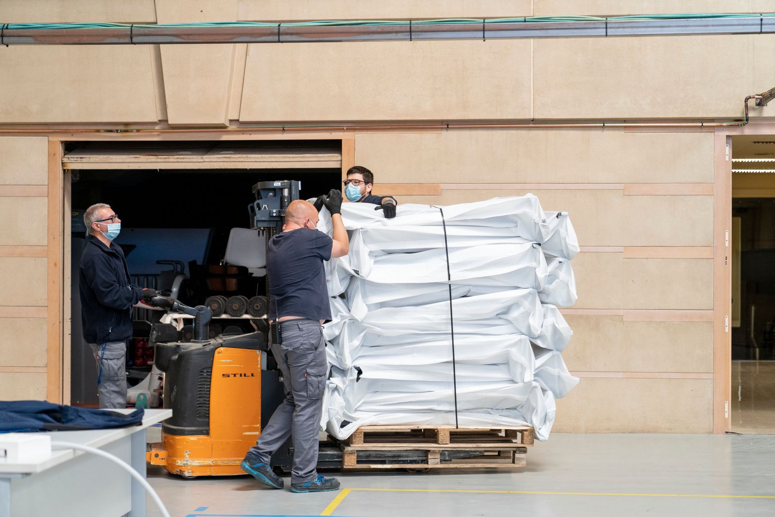 Treballadors amb màscares i guants traginen palets de material a un dels pavellons de l’INEFC