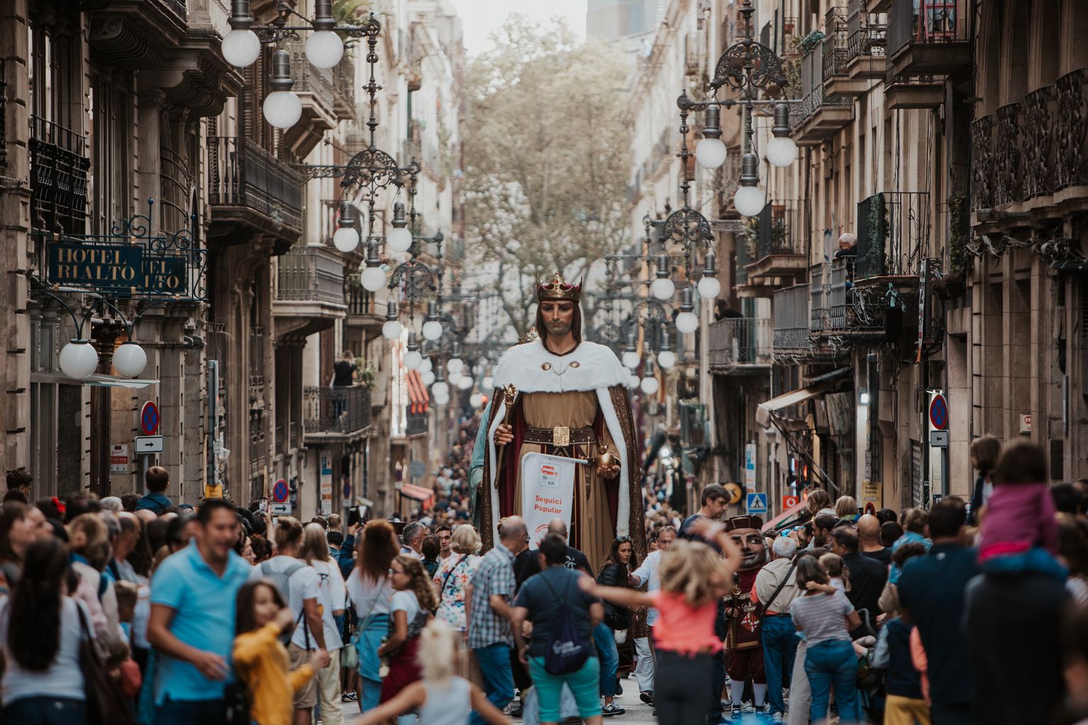 El Gegant de la Ciutat, Jaume I, desfila pel carrer de Ferran envoltat de famílies amb nens que gaudeixen de la Cavalcada de la Mercè i d’altres elements de la imatgeria festiva barcelonina, com un dels Nans Macers