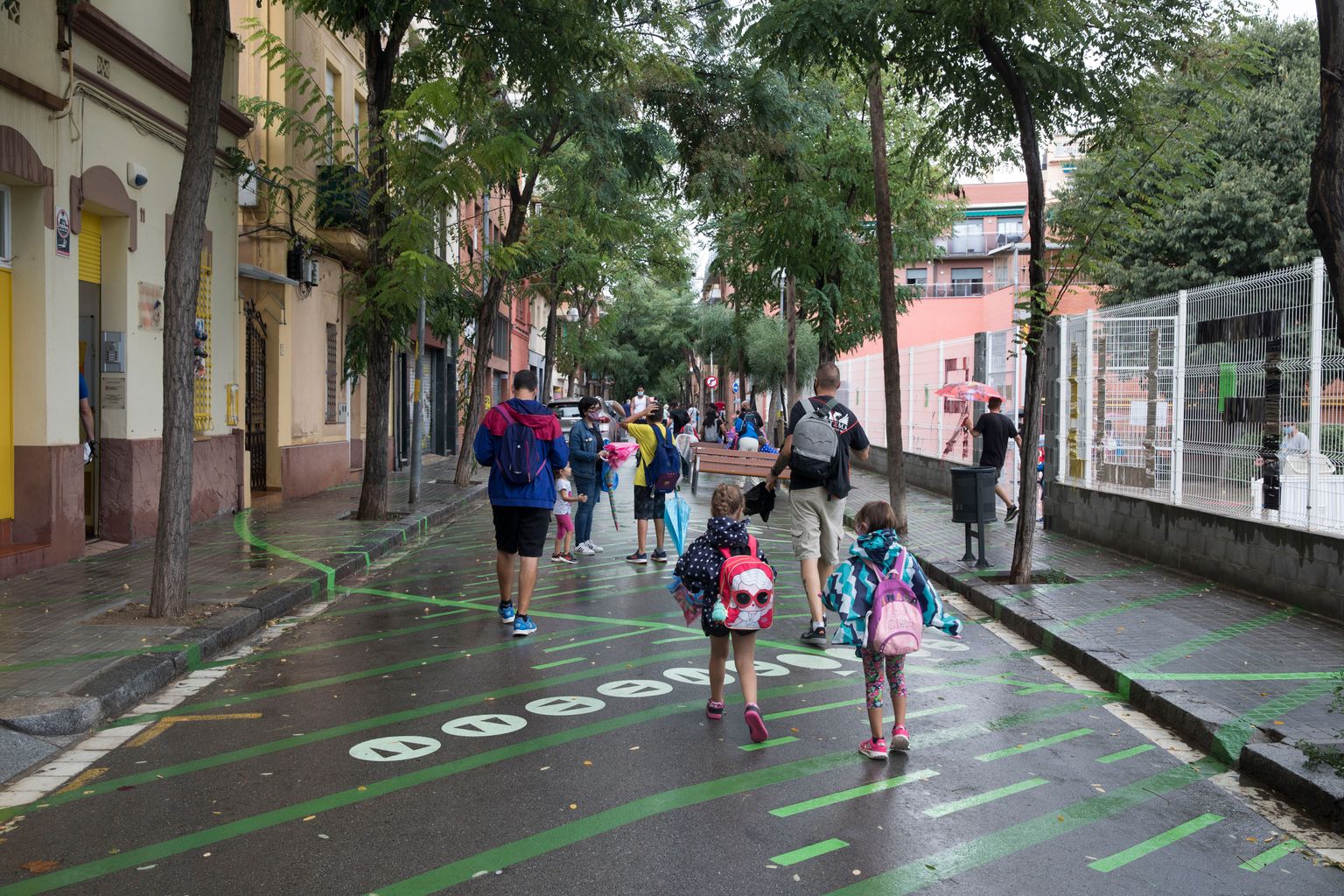 Nens caminant en direcció al col·legi per la zona pacificada davant de l’entrada que hi ha al carrer de les Acàcies de l’Escola Doctor Ferran i Clua durant un dia plujós