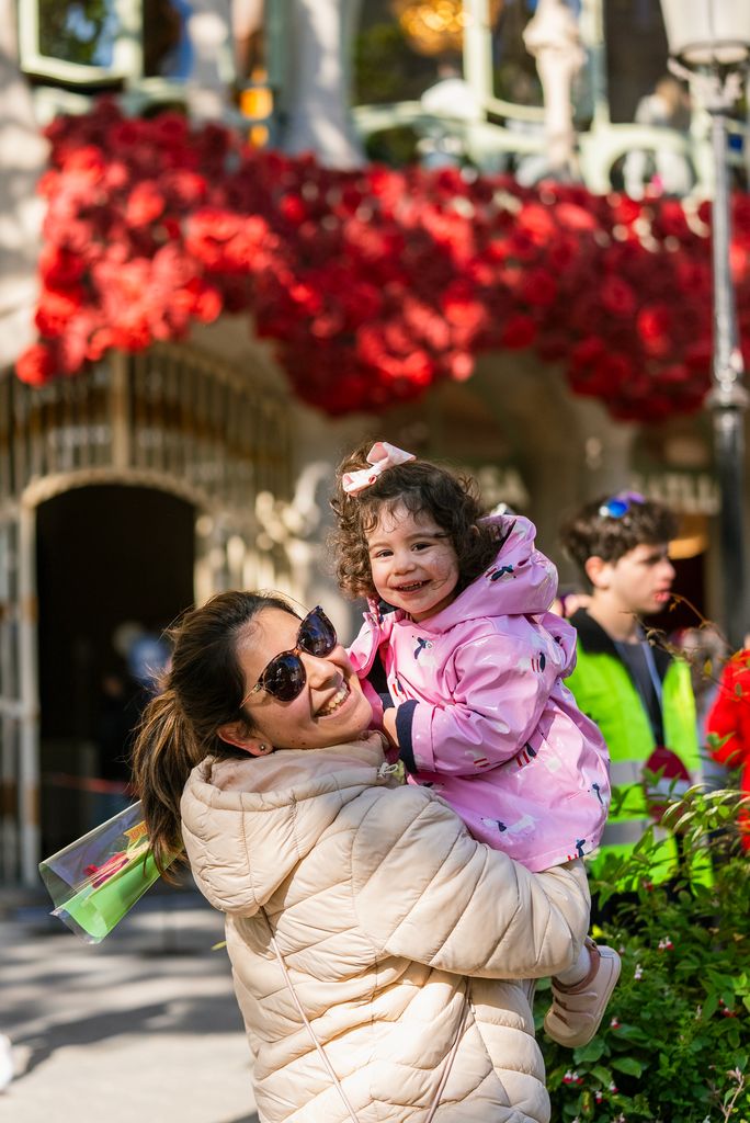 Una madre con su hija en brazos delante de la Casa Batlló, que tiene la fachada adornada con rosas para conmemorar Sant Jordi.