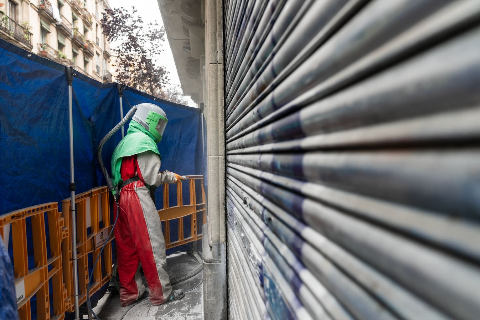 Un trabajador con el traje de protección y el espacio a su alrededor protegido limpia unas pintadas de una pared del Raval.