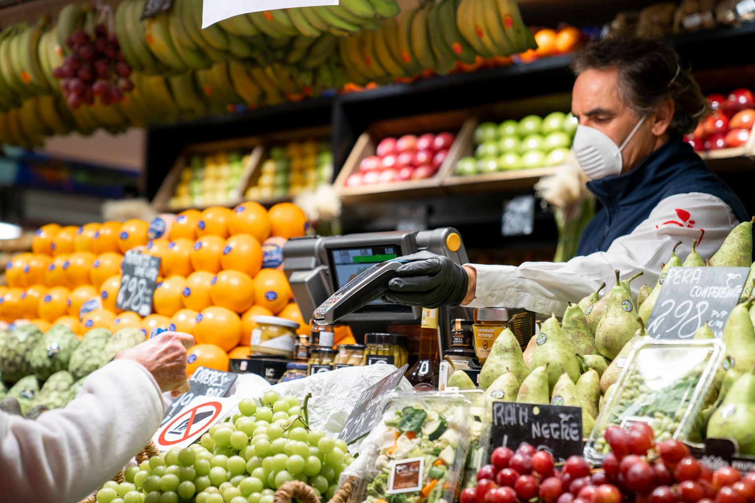 Mercat del Ninot. Un botiguer li acosta el datàfon a una clienta perquè pugui pagar amb targeta de crèdit la compra a la seva parada de fruites i verdures