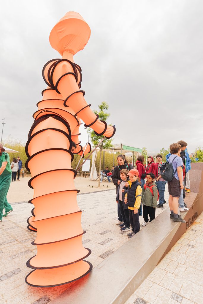 Un ninot gegant de color taronja i nens mirant-lo en la festa d'inauguració del parc de les Glòries