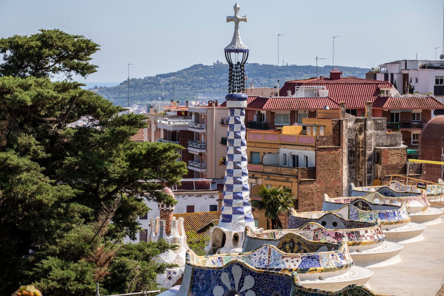 Banco del mirador del Park Güell recubierto con trencadís. De él sobresale la torre del edificio de administración.
