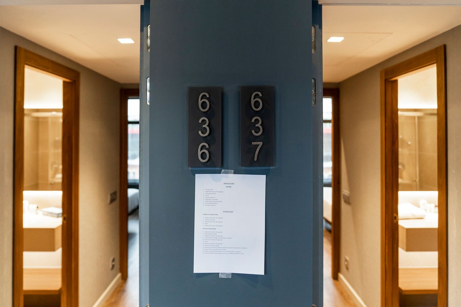 Habitacions de l’Hotel Catalonia Plaza encara per ocupar i amb les portes obertes, on es poden veure els banys i els llits al fons. A l’espai entre les dues habitacions es pot llegir el número de cada una d’elles i hi ha penjat un protocol d’actuació