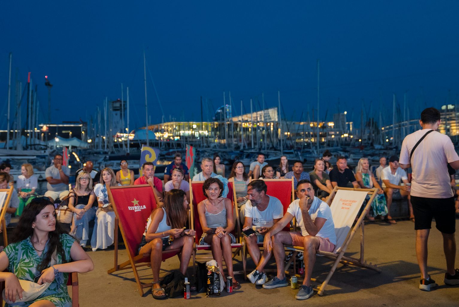 Públic assegut a cadires i gandules de la Race Village seguint un concert ofert en el marc de la Regata Cultural