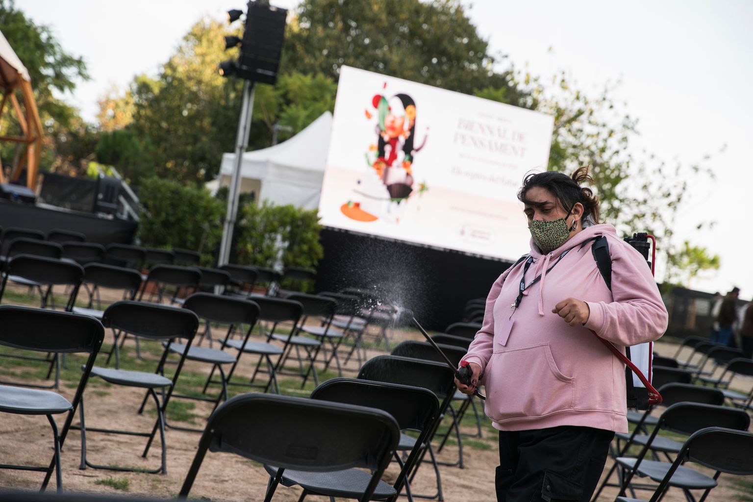 Una dona de l'organització ruixa amb un desinfectant les cadires abans de l'arribada del públic als jardins del Doctor Pla i Armengol