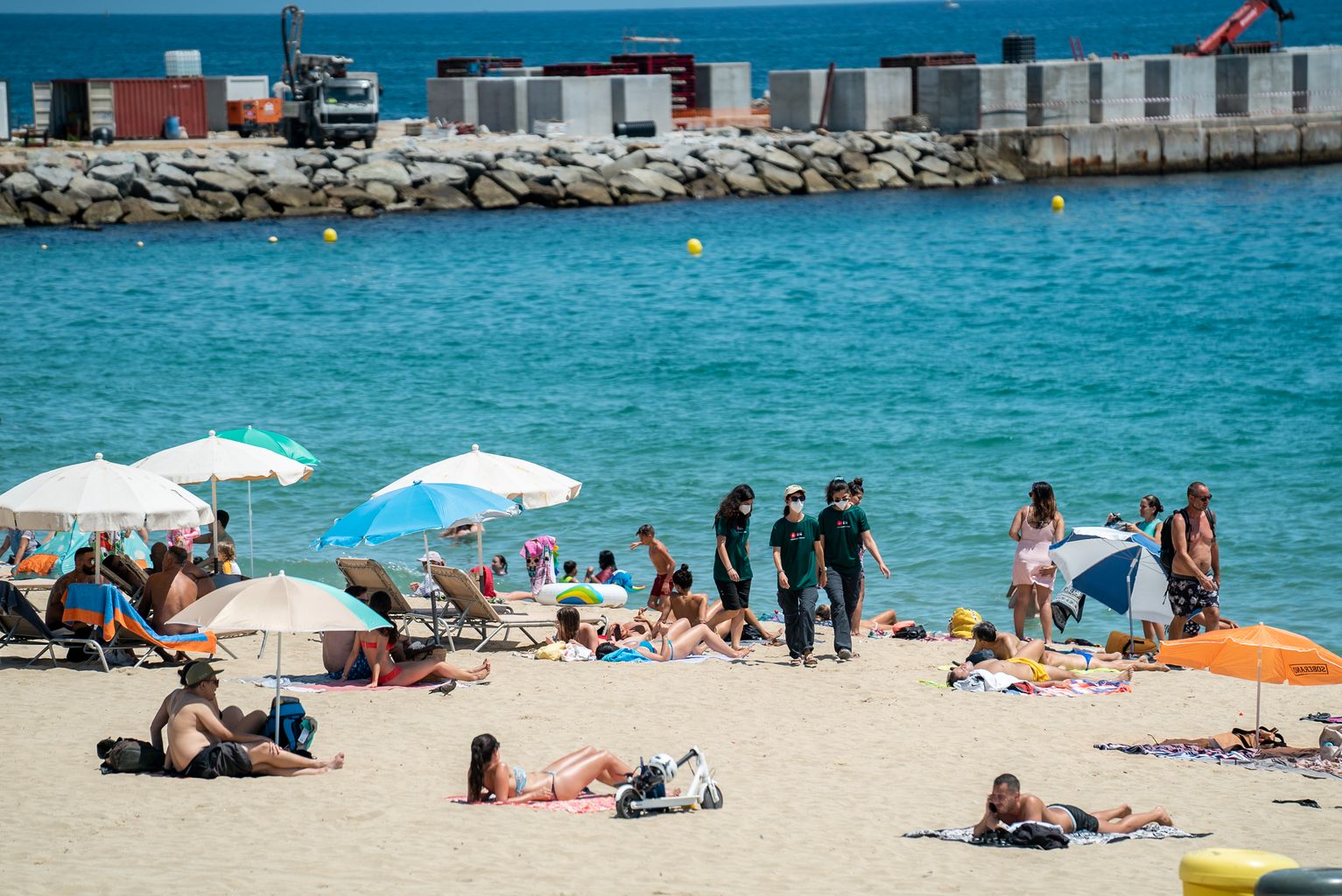 Informadores caminen per la sorra de la Platja del Bogatell per informar els banyistes de les mesures covid-19
