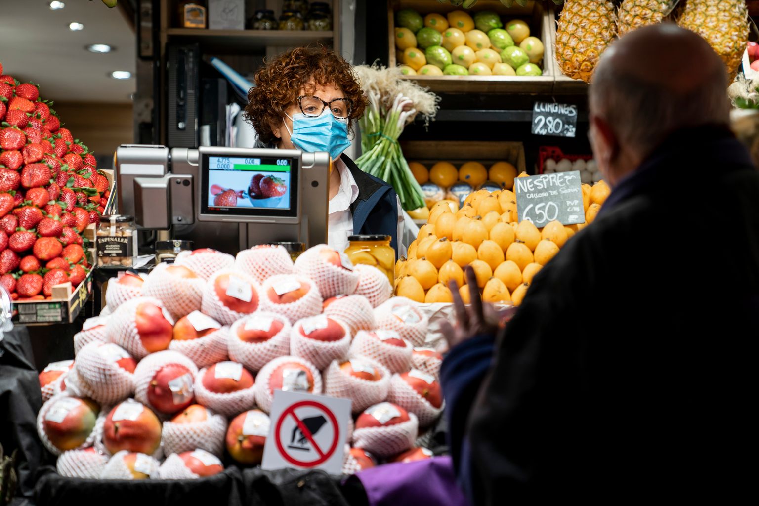 Mercat del Ninot. Un home gran davant d’una parada li indica a la dependenta amb mascareta el nombre de peces que vol.