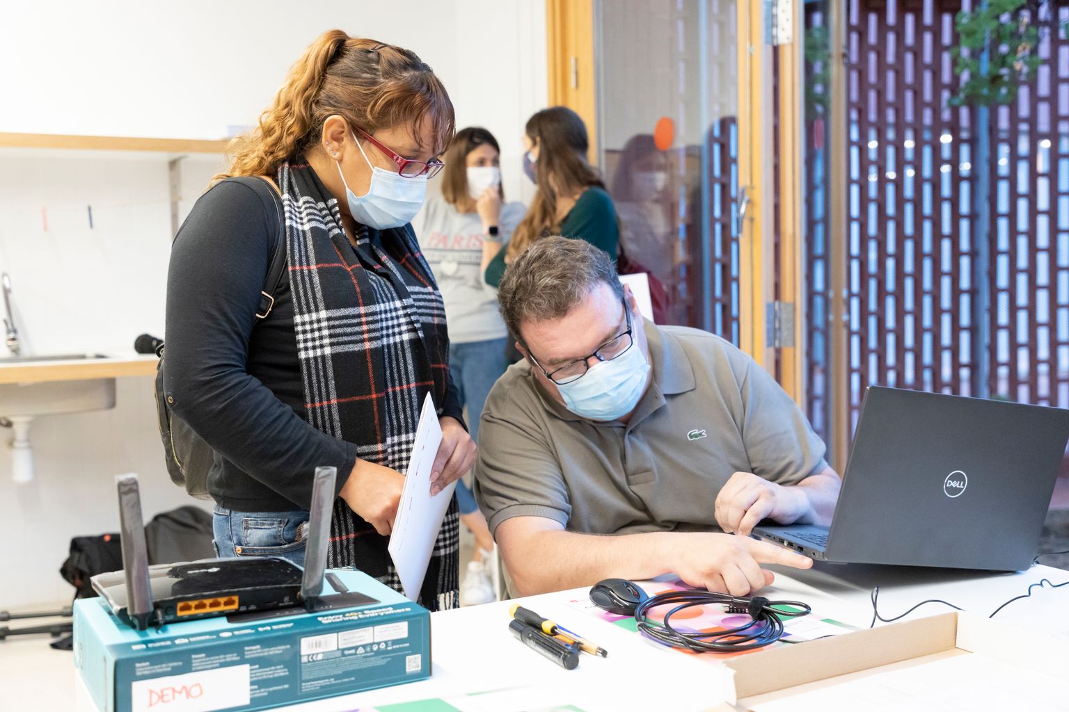 Un responsable del projecte 'Connectem Barcelona' mostra a una usuària com connectar l'equipament informàtic que li han lliurat