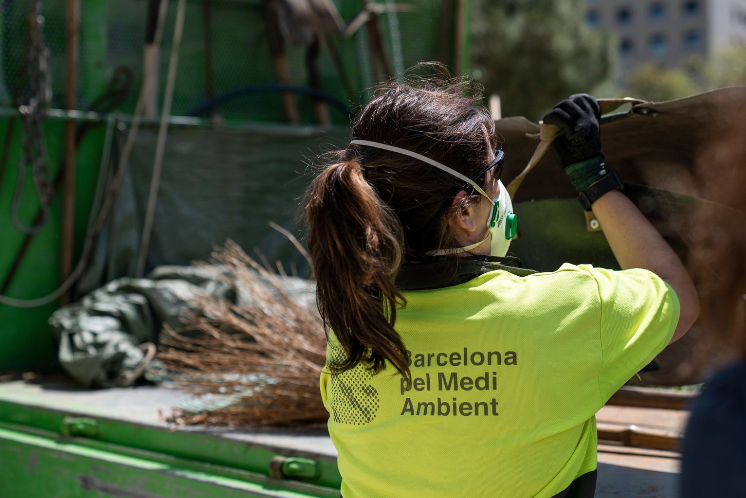 Una de les jardineres amb mascareta agafa un cistell de darrere del camió de Barcelona pel Medi Ambient