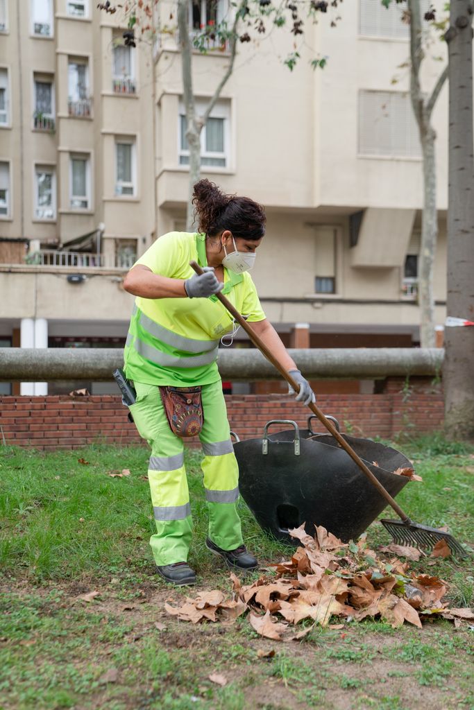 Una trabajadora del Servicio de Limpieza amontona hojas secas con la ayuda de un rastrillo