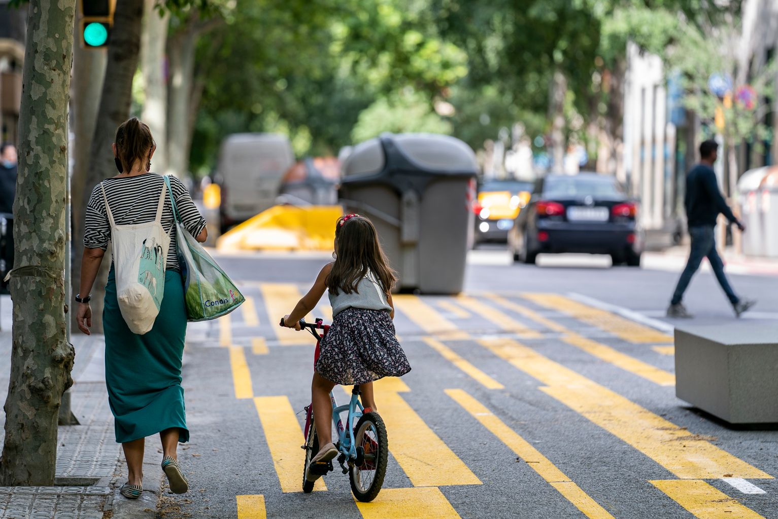 Una familia, una madre cargada con bolsas y una niña en bicicleta, utiliza la ampliación para peatones de la calle del Consell de Cent y pasa al lado de los bancos nuevos