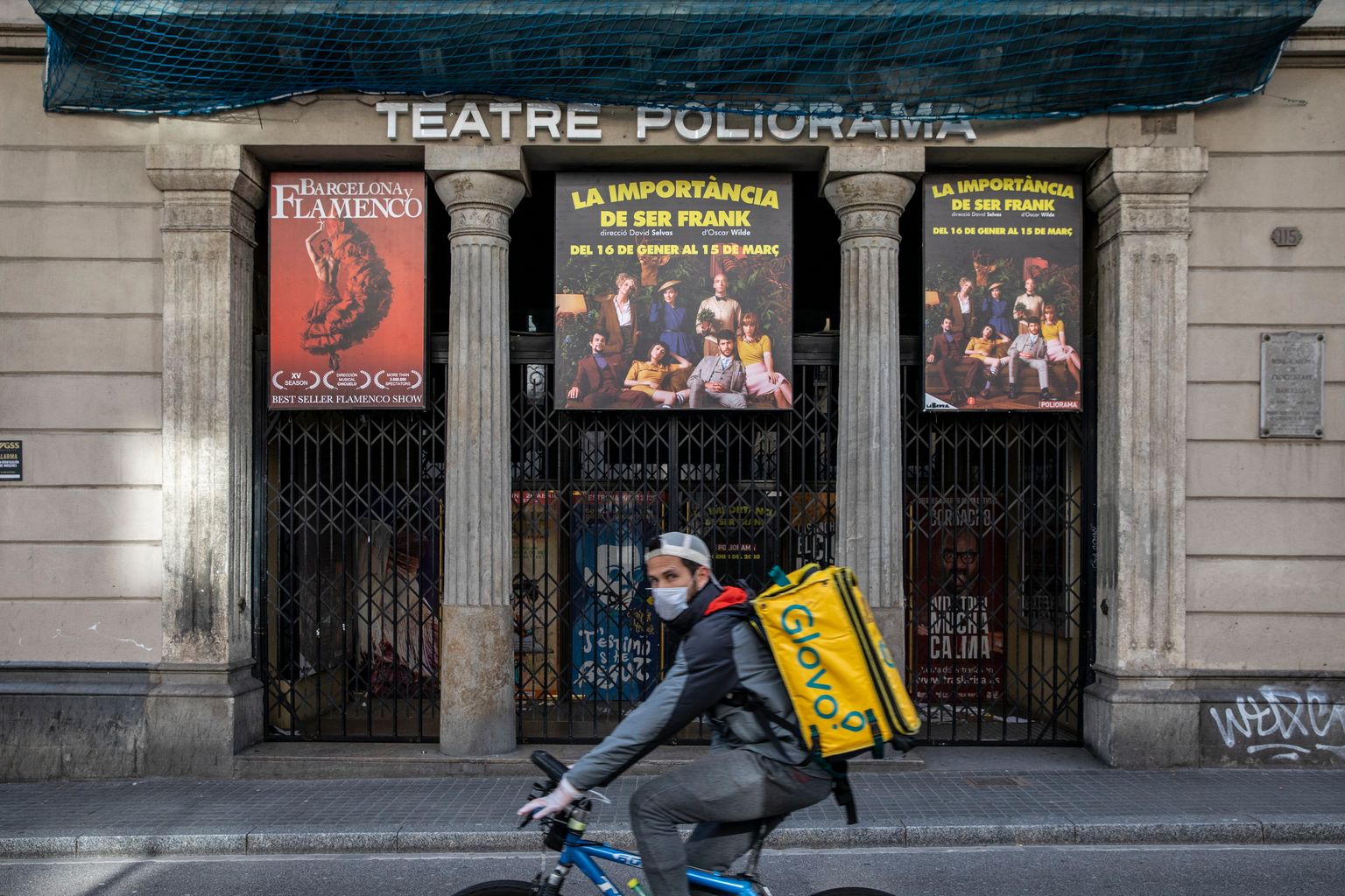 Repartidor de Glovo en bicicleta transportant alguna comanda i portant una mascareta i guants