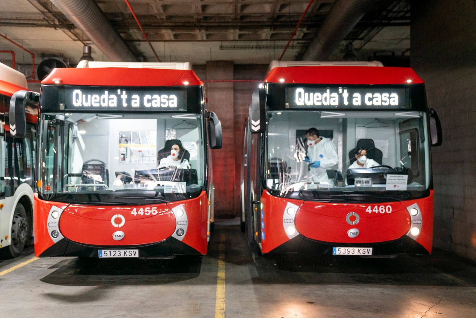 Dos autobuses en las Cocheras de Horta con el letrero “Queda’t a casa”, preparados para transportar a pacientes de hospitales a los espacios de confinamiento. Dentro se ven los conductores protegidos y algún compañero voluntario de TMB más