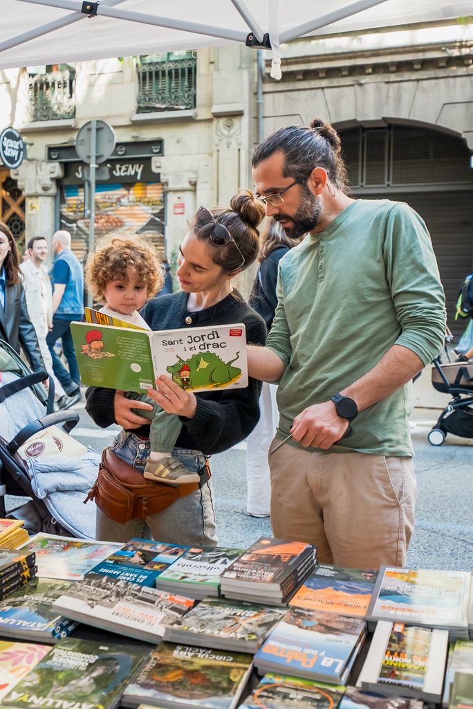 Un home, una dona i un nen petit miren un llibre infantil sobre la llegenda de Sant Jordi