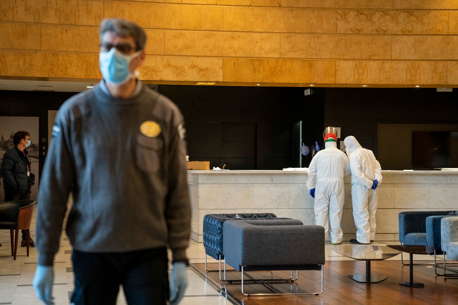Personal de seguridad y sanitario en la recepción del Hotel Catalonia Plaza. El guardia de seguridad lleva guantes y mascarilla y los sanitarios llevan un mono impermeable, guantes y mascarilla
