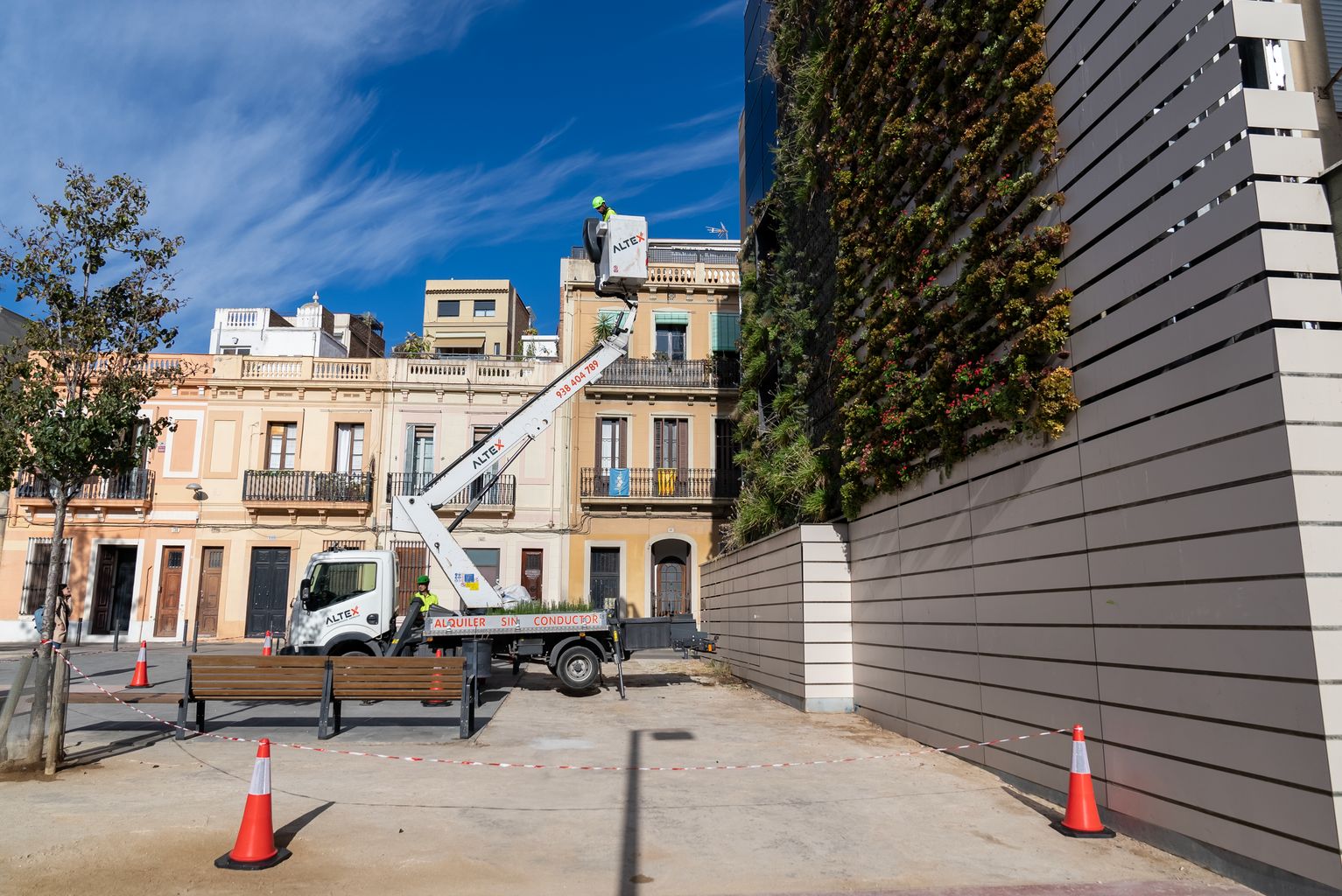 Pla general de la plaça de les Dones del 36, on hi ha el jardí vertical en el moment en què uns treballadors enfilats en una grua treballen en el jardí vertical.