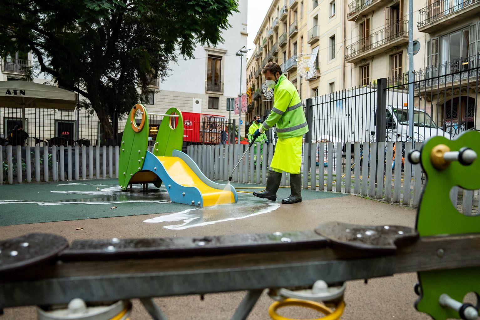 Un trabajador del Servicio de Limpieza rocía con agua a presión y jabón el pavimento del área de juegos infantiles de la plaza de la Vila de Madrid