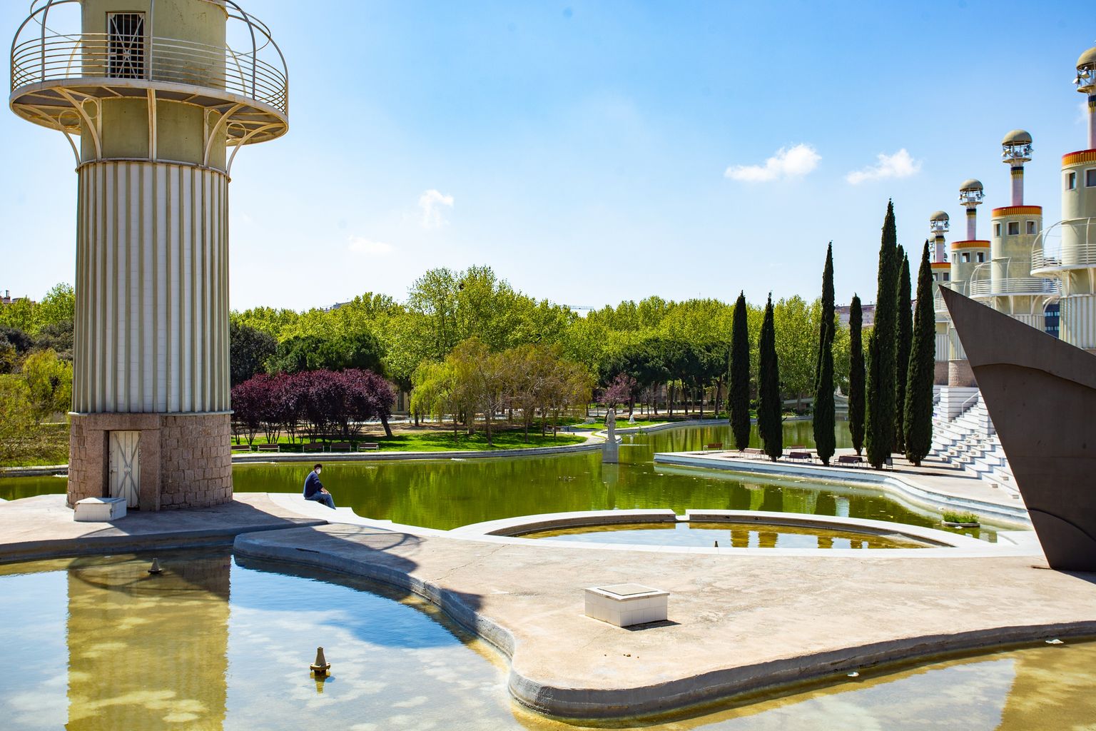 Parc de l’Espanya Industrial amb una persona asseguda al costat de les fonts sense aigua. Districte de Sants-Montjuïc. Barri de Sants. 
