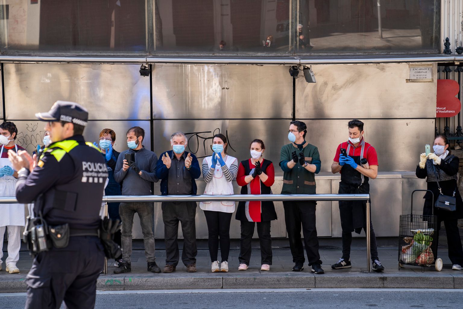 Agent de la Guàrdia Urbana aplaudint als paradistes del Mercat d'Hostafrancs que se'ls miren des de la vorera