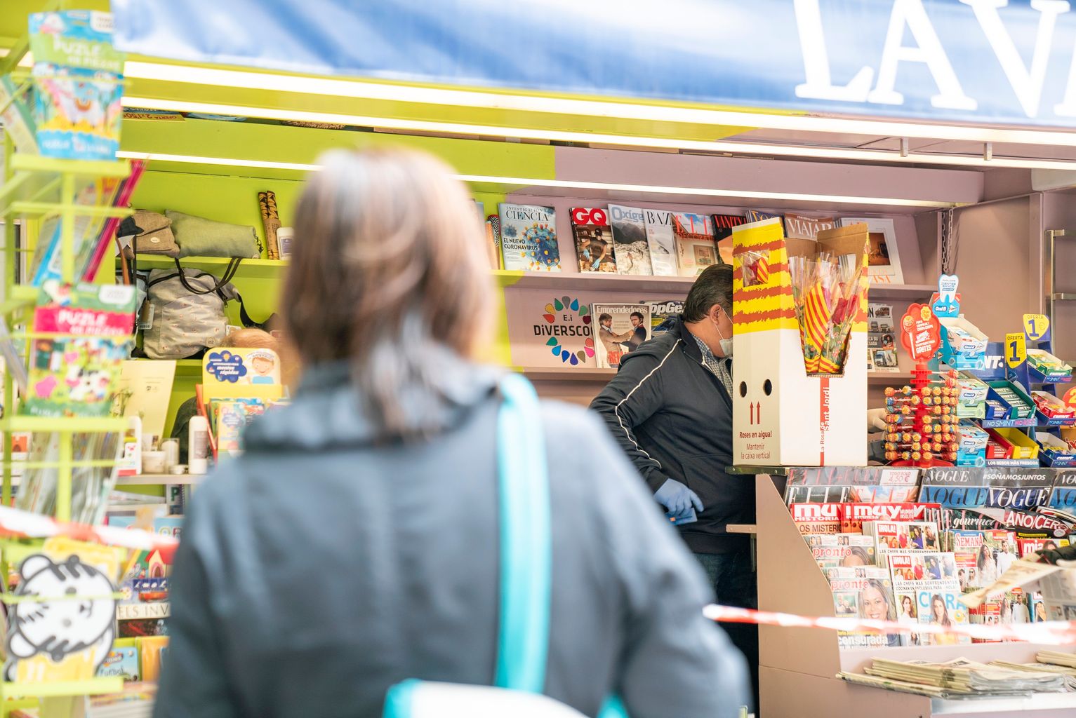 Una dona s’apropa al quiosc on hi ha una caixa de roses de les distribuïdes per l’Ajuntament als quioscos de Diverscoop amb motiu de Sant Jordi