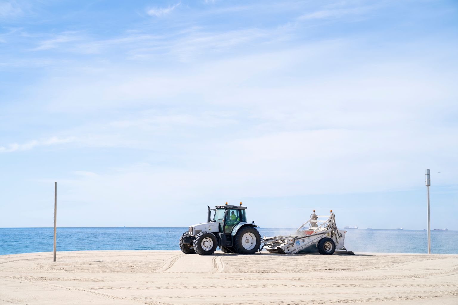 Un tractor prepara la sorra de la platja del Bogatell