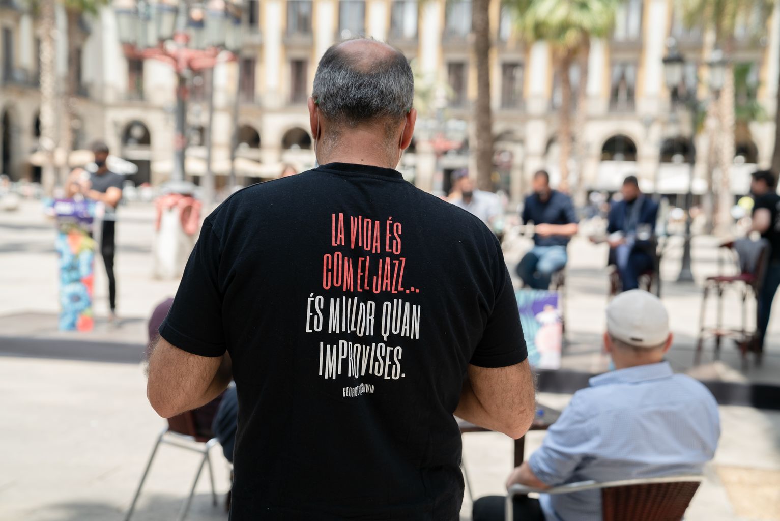 Un dels assistents a l’acte de presentació del programa Àgora Rambles a la plaça Reial mostra una samarreta amb el lema “La vida és com el jazz, és millor quan improvises”