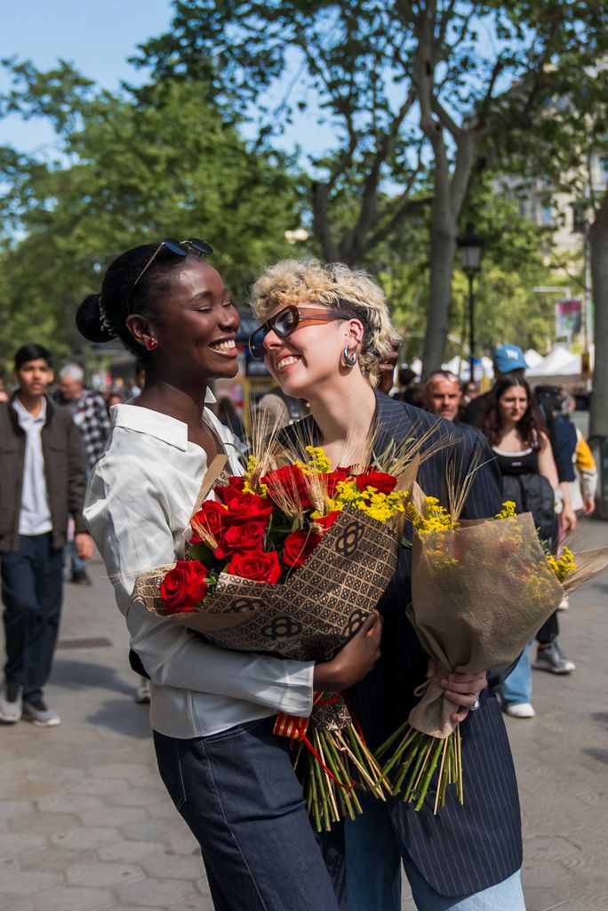 Dos chicas se abrazan y ríen con ramos de rosas en las manos el Día de Sant Jordi