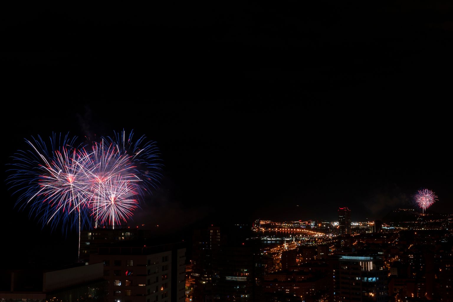 Vistes de la ciutat amb els focs d'artifici del piromusical des de dos punts, l'Espigó de Bac de Roda a Sant Martí i el Castell de Montjuïc, a Sants-Montjuïc